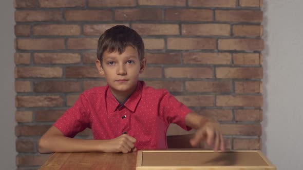 Child Sitting at the Desk Holding Flipchart with Lettering Ok on the Background Red Brick Wall