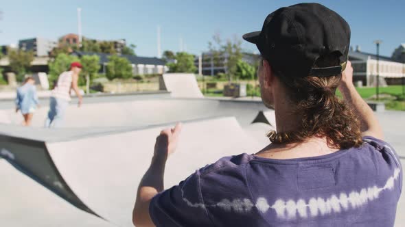 Back view of caucasian man on sunny day, skateboarders in background