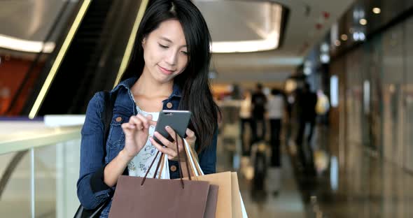 Woman holding shopping bags and using mobile phone in plaza 