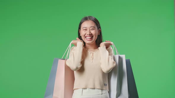 Asian Shopping Woman Holding Shopping Bags Up Being Happy And Smiling In Front Of Green Screen