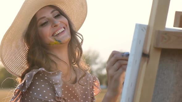 Artist girl paints with brushes on canvas in a field at sunset