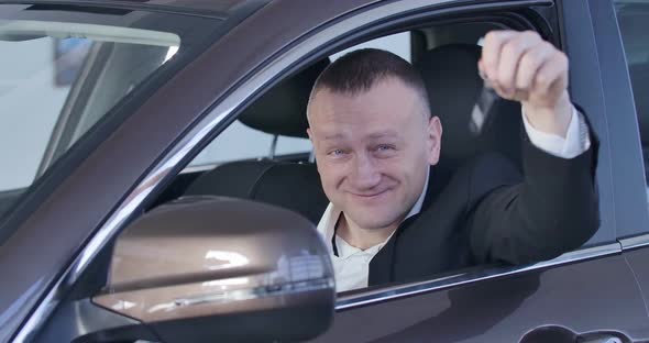 Close-up of Satisfied Caucasian Man Showing Car Keys and Thumb Up As Sitting on Driver's Seat in New