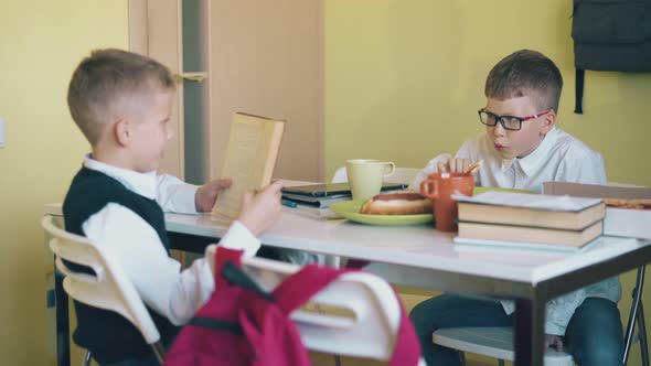 Hungry Boy Eats Pizza and Friend Reads Book at White Table