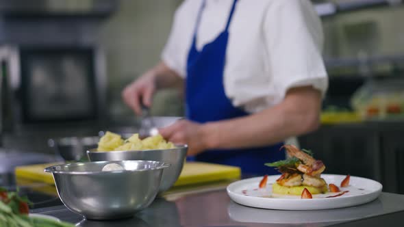 Cooked Seafood and Raw Ingredients in Commercial Kitchen with Unrecognizable Male Cook Mixing in