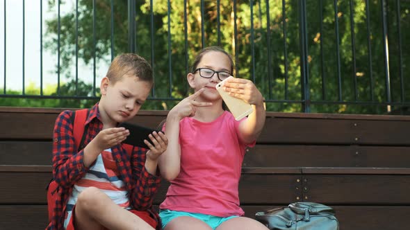 The Older Sister and Brother Are Sitting on the Street, Looking at Smartphones.