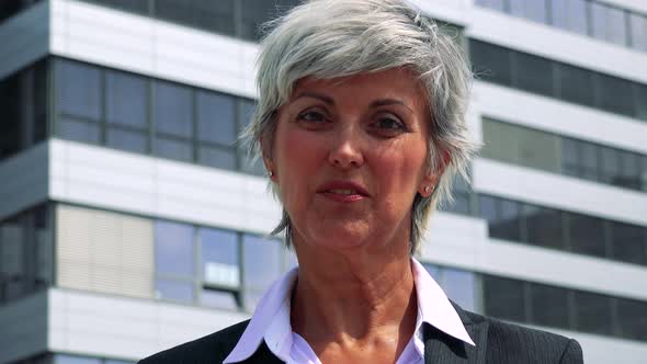 Business Middle Age Woman Smiles To Camera - Company Building in the Background - Closeup