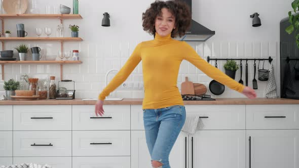 Happy Hispanic Curly Woman Listening to Music and Dancing at Home in the Kitchen