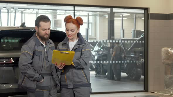 Beautiful Female Car Mechanic Discussing Work with Male Colleague at the Garage