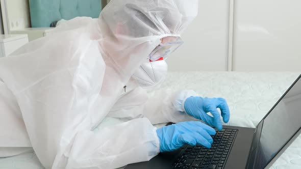 Medical Worker in Protective Suit Mask and Gloves Lying at Home and Working on Laptop Computer