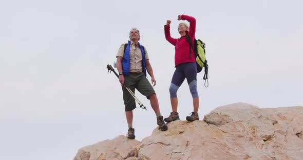 Senior hiker couple with backpack and trekking poles standing with their arms wide open on the rocks