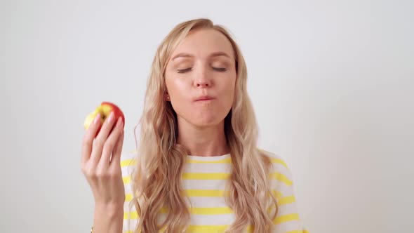 Young Attractive Woman on a White Background Bites an Apple