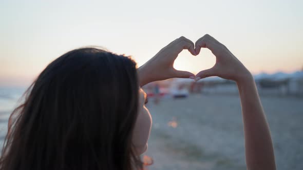 Happy Summer, Girl Enjoys Sunny Weekend and Shows Her Heart with Her Hands Background of Sea on