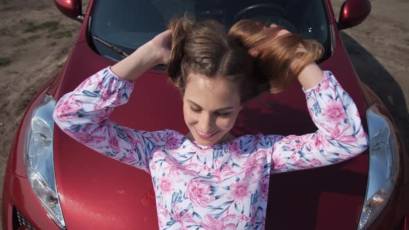 Beautiful Woman Straightening Her Hair Stacked on the Hood of a Red Car