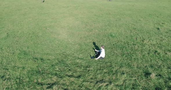 Low Orbital Flight Around Man on Green Grass with Notebook Pad at Yellow Rural Field