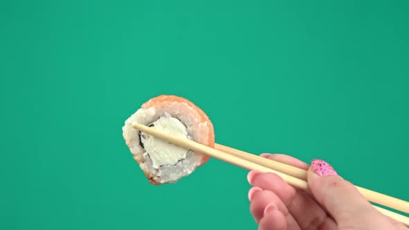 Female Hands Hold Japanese Chopsticks with Sushi Rolls on Green Background