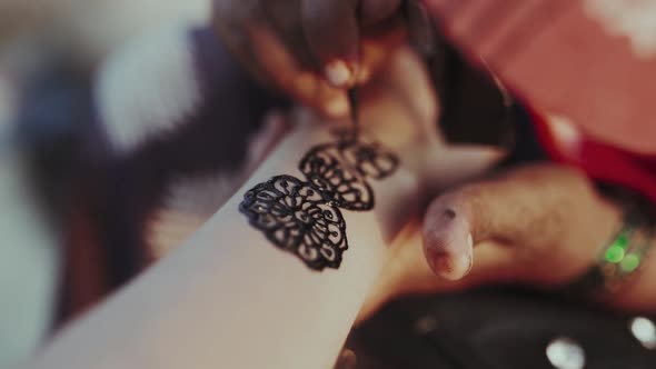 Close up Henna artist applies a henna tattoo on woman's arm.