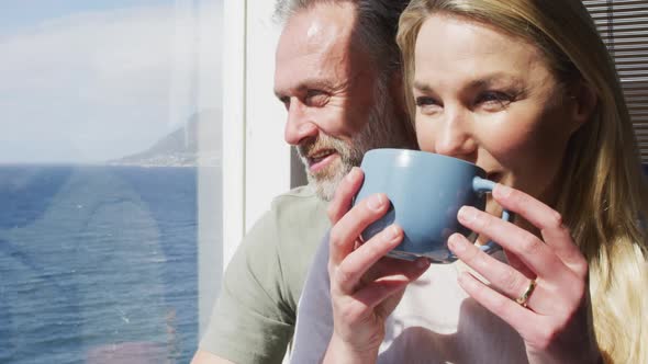 Happy caucasian mature couple drinking coffee and talking in sunny living room