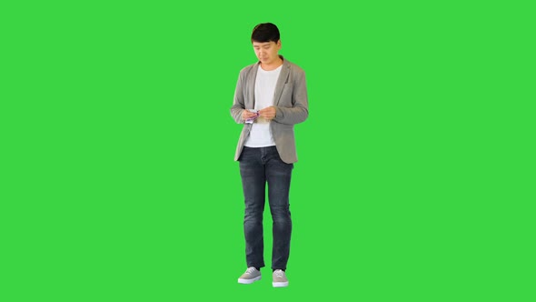 Young Asian Man Counts Money and Puts Them Into Pocket on a Green Screen Chroma Key