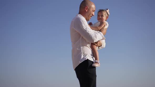 Side View of Happy Smiling Father and Baby Daughter Talking Dancing at Background of Clear Blue