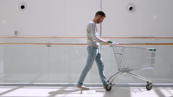 Beautiful Young Man Having Fun Riding on Shopping Cart at Supermarket.