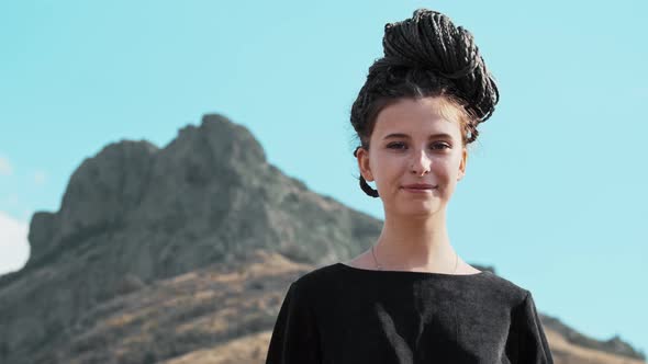 Young Woman with Dreadlocks Waving with Her Hand on the Background of Mountains