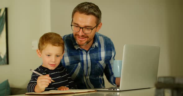 Father watching son doing homework at table 
