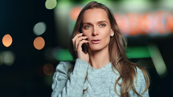 Smiling Casual Woman Talking Smartphone at Night Downtown
