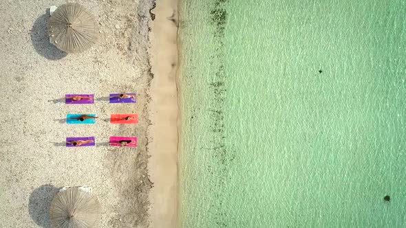 Aerial view of group of people in yoga pose on colourful mats on the beach.