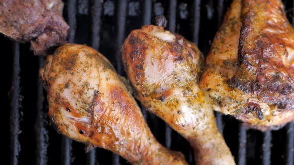 Drumstick chicken legs and lamb chops on a barbecue grill. Flames igniting and flaring from under th