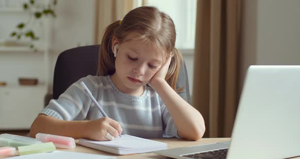 Portrait of Focused Preschool Girl Sits at Home, Writes Task in Notebook with Pen, Does Homework