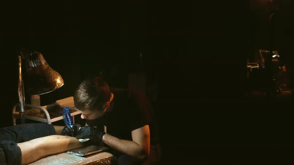 Tattoo Artist Working with Clients Leg Under Lamp