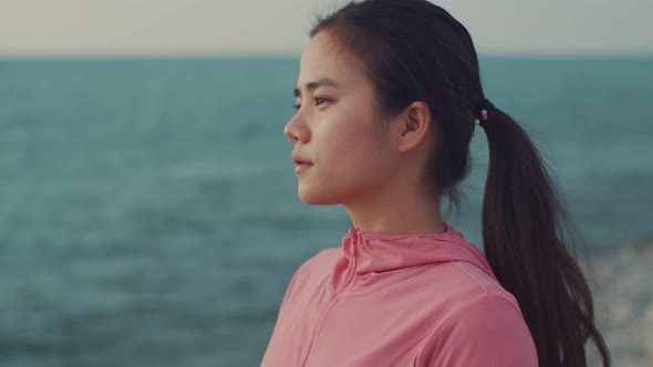 A beautiful Asian woman runner looks at the sea view while standing on the beach.