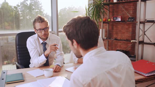 Male Job Applicant in White Shirt Speaking with Caucasian Boss in Glasses Sitting at Table with