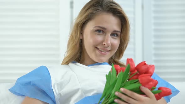 Happy Female Clinic Patient Holding Red Tulips in Hands, Recovering After Labor