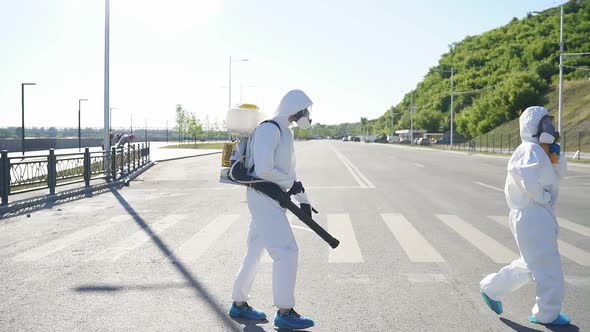 Professional Disinfectors in Protective Hazmat Suit Walking Through City Streets