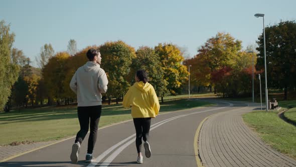 Man and Woman Running on a Track at the City Park in Sunny Autumn Morning