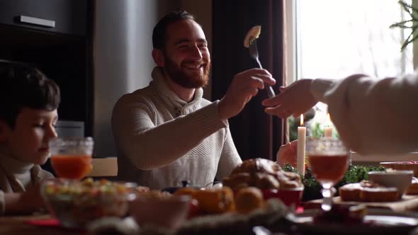 Lowangle View of Loving Young Woman Passes to Husband Piece of Holiday Turkey Sitting at Festive