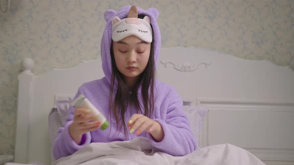 Asian Woman in Sleeping Mask Using Hand Cream Sitting in Bed