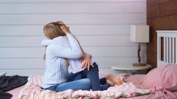 Barefoot Child Girl Gives Big Hug to Her Mother Sitting on Bed in Bedroom at Home Interior Full Shot