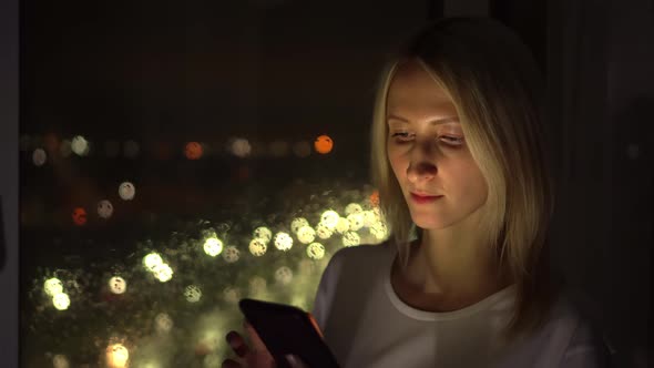 a woman uses a smartphone. The light from the phone illuminates the face.