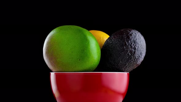 Mango Avocado and Orange Rotate in the Red Plate on a Black Background