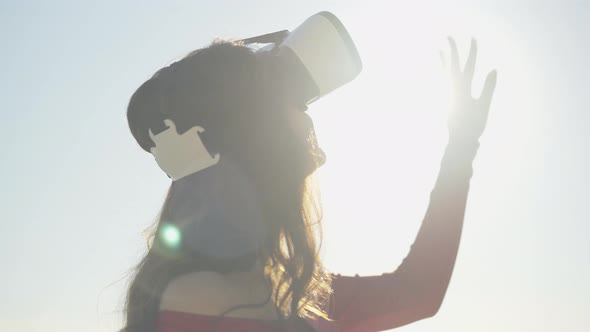 Close-up of Happy Young Brunette Woman in VR-glasses Standing in Sunrays Outdoors. Portrait of