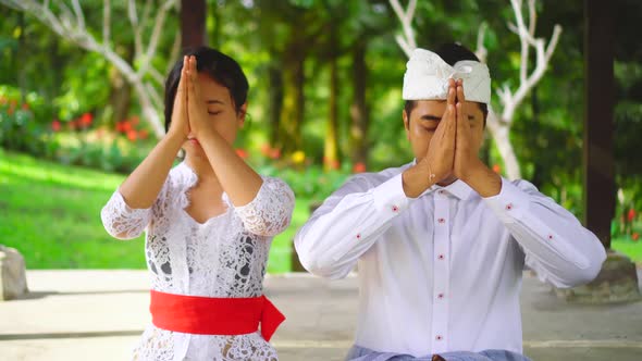 Hindu family in Bali pray in temple. Balinese couple with hands at forehead. Culture of Indonesia