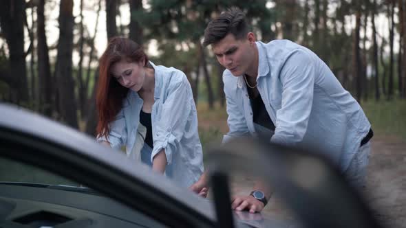 Thoughtful Concentrated Couple Choosing Route Leaning at Car Hood in Forest