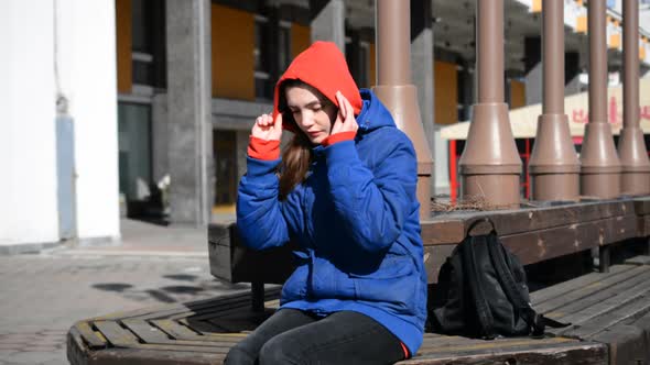 Beautiful Hipster Girl Sits on a Bench in the City and Freezes