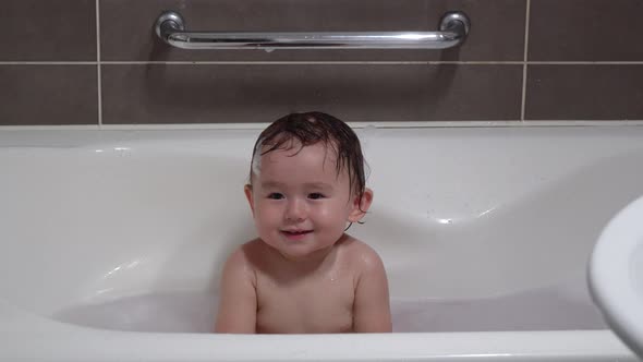 Cheerful Mixed Asian Toddler one-year-old Baby Showing Toothy Smile While Bathing In A Foamy Bathtub