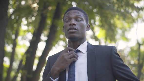 Close-up of Young Handsome African American Man Adjusting Necktie in Summer Park and Leaving