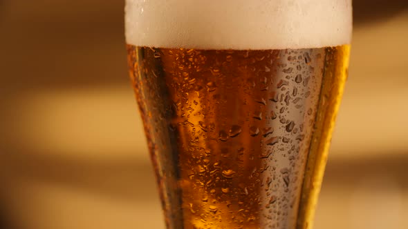 Closeup of Rotating Fresh Beer with Abstract Golden Background and Drops on Glass