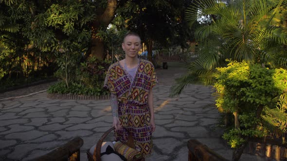 Tracking shot of a stunning caucasian woman in a native outfit walking through a tropical garden