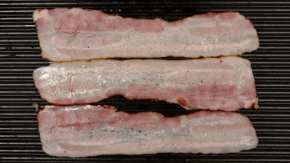 Frying A Strips Af Bacon On A Black Pan